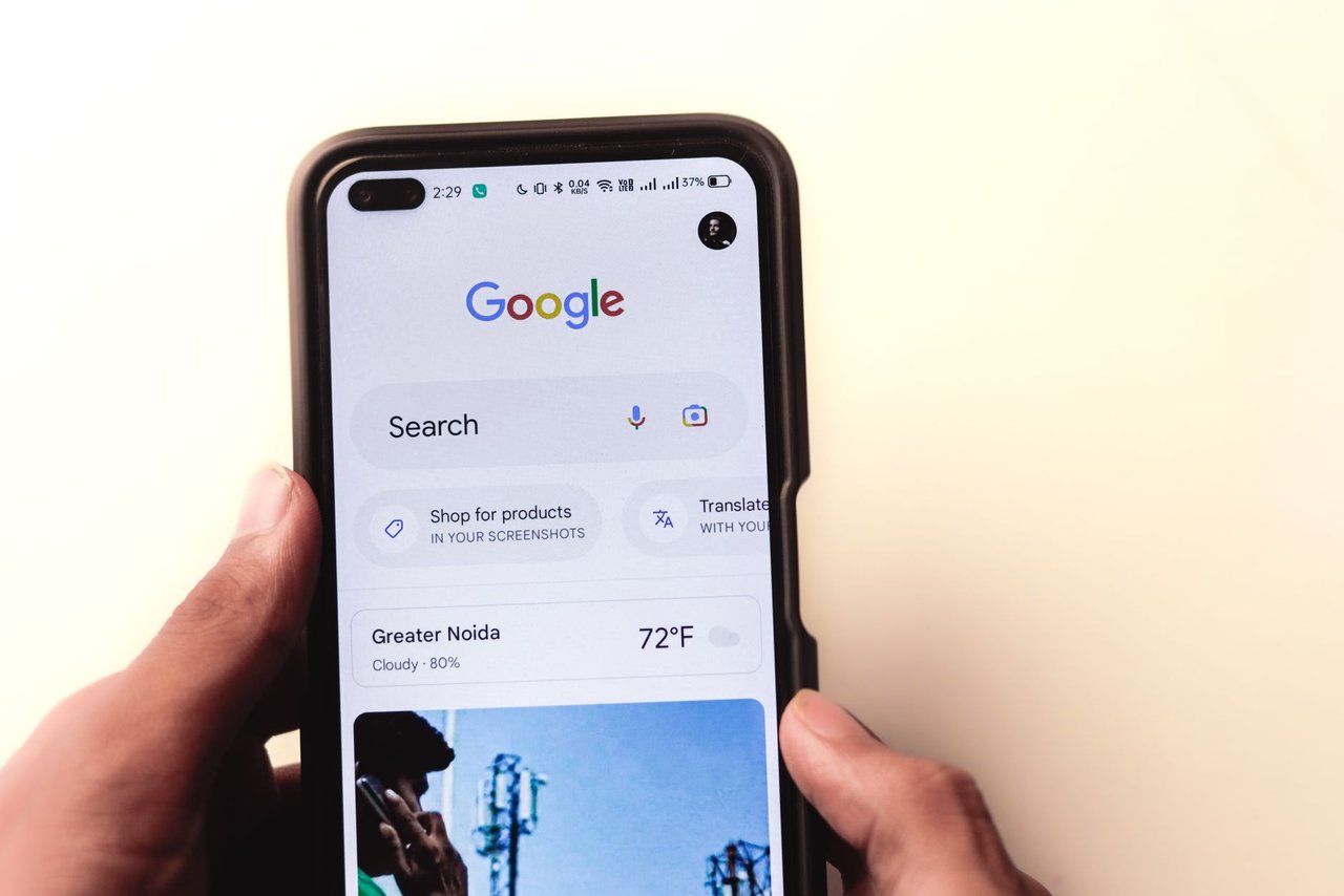 Mão segurando um smartphone com a página de busca do Google exibida na tela.