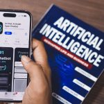 Smartphone exibindo um aplicativo de inteligência artificial, com um livro sobre tecnologia de IA ao fundo.