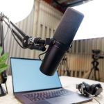 Estúdio de podcast com microfone profissional, laptop e fones de ouvido preparados para uma gravação.