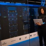Profissional monitora servidores com um laptop em uma sala de data center.