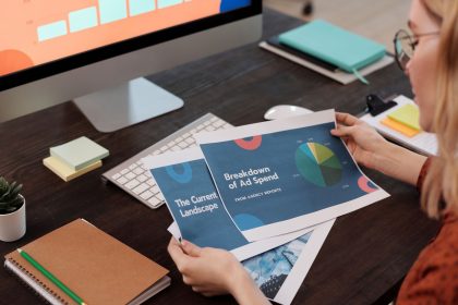 Profissional analisa documentos e gráficos de marketing em uma mesa com computador.
